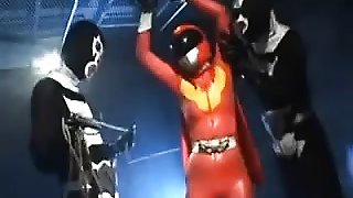 Sexy Super Hero in orange latex is strung up and tortured b